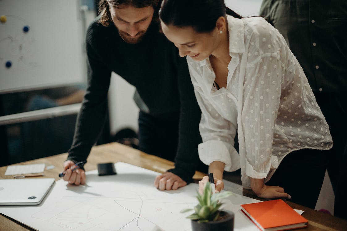 Free Man and Woman Leaning on Table Staring at White Board on Top of Table Having a Meeting Stock Photo